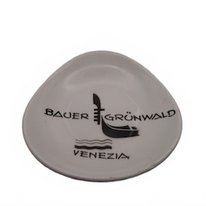 May include: A white, triangular-shaped ceramic dish featuring a black graphic of a gondola and the text "BAUER GRÜNWALD" above the image and "VENEZIA" below the image, with wavy lines separating the gondola graphic from the text.