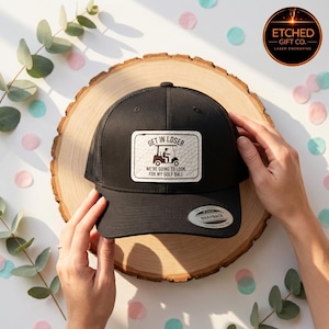 May include: Black trucker hat with a white patch featuring the text "GET IN LOSER WE'RE GOING TO LOOK FOR MY GOLF BALL" and a golf cart graphic. The hat has a mesh back and a snapback closure.