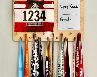 Könnte beinhalten: Ein helles, an der Wand montiertes Holzregal mit der Gravur "EARNED, NOT GIVEN" an der Oberseite. Es verfügt über einen Clip für eine Startnummer 1234, ein Whiteboard mit der Beschriftung "Next Race:" und "Goal:" sowie Haken für mehrere bunte Laufmedaillen.