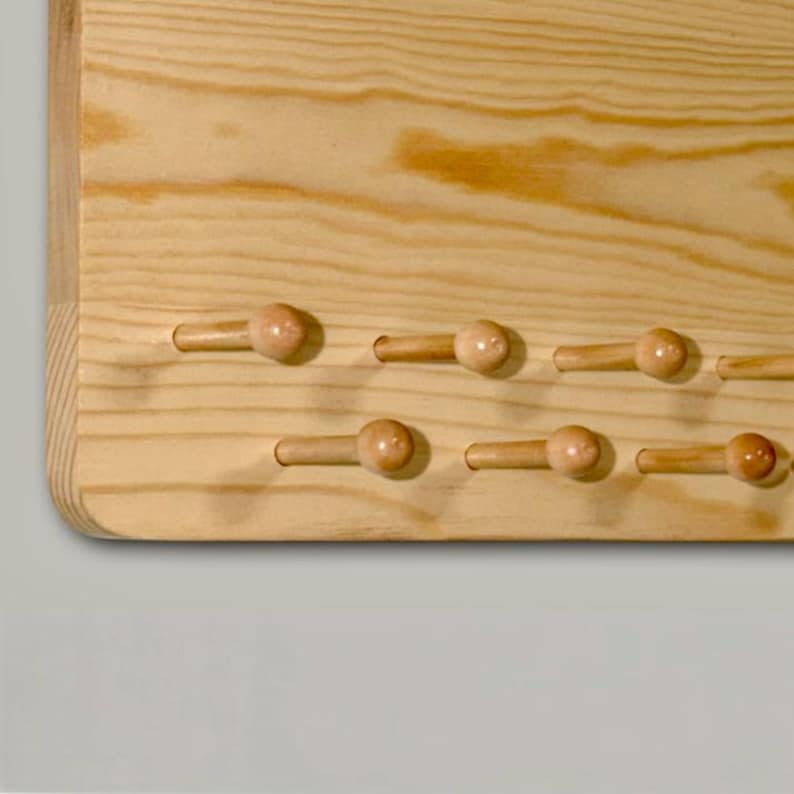 K&ouml;nnte beinhalten: Ein helles Holzwandregal mit nat&uuml;rlicher Maserung und zwei horizontalen Reihen abgerundeter Haken. Das Regal ist aus glattem, unbehandeltem Holz gefertigt und zeigt die organische Textur sowie die hellbraunen Farbt&ouml;ne des Materials.