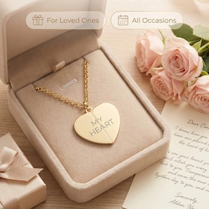 May include: A gold-colored heart pendant necklace in an open beige jewelry box. The pendant is engraved with the words "MY HEART". The image also includes a gift box, pink roses, and a handwritten letter.