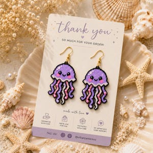 May include: A pair of beaded jellyfish earrings on a display card with the text thank you SO MUCH FOR YOUR ORDER and made with love. The earrings feature purple, pink, and white beads with gold-toned hooks. The card includes icons and text.