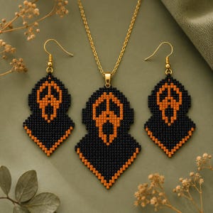 May include: A jewelry set consisting of a necklace and two matching earrings, all crafted from small black and orange beads arranged in a pixelated ghost mask pattern. The earrings feature gold-toned hooks, and the pendant hangs on a gold chain.