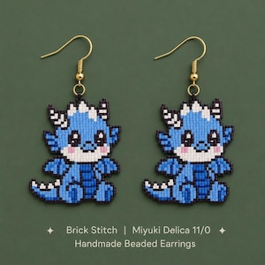 May include: A pair of handmade beaded earrings featuring a blue dragon design crafted with brick stitch and Miyuki Delica 11/0 beads. The dragon has a light blue body, white accents, and pink cheeks, suspended from gold-toned metal earring hooks.