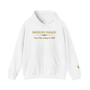 Könnte beinhalten: Weißer Kapuzenpullover mit Fronttasche und Kordelzugkapuze. Auf der Vorderseite des Hoodies steht in Gold der Text "MISSION FAILED" über "That Was Going So Well". Auf dem rechten Ärmel befindet sich ein kleines goldenes Emblem.