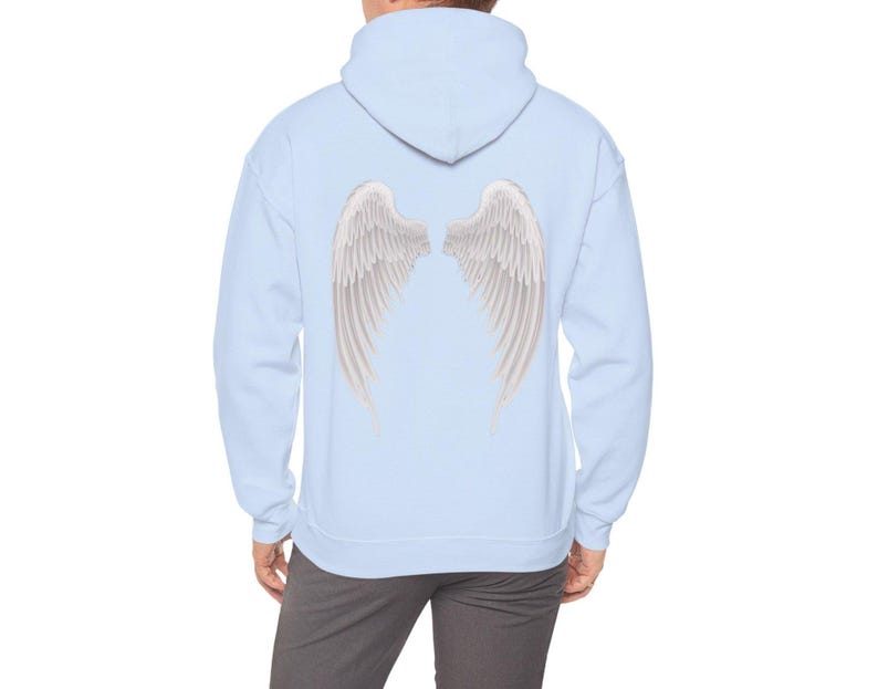 May include: A light blue hoodie featuring a detailed illustration of white angel wings on the back. The wings have a layered feather design with subtle shading, creating a realistic appearance. The hoodie has a hood and a relaxed fit.