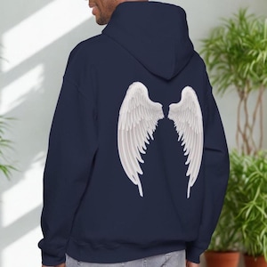 May include: A navy blue hoodie featuring a large white angel wing design on the back. The wings are detailed with individual feathers. The hoodie has a hood and a relaxed fit, suitable for casual wear.