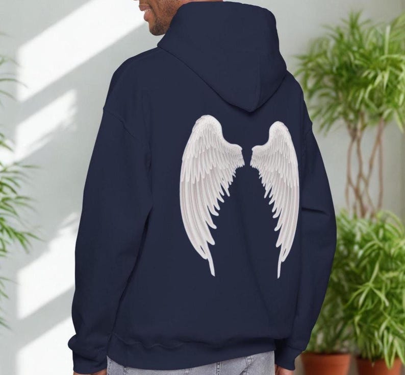 May include: A navy blue hoodie featuring a large white angel wing design on the back. The wings are detailed with individual feathers. The hoodie has a hood and a relaxed fit, suitable for casual wear.