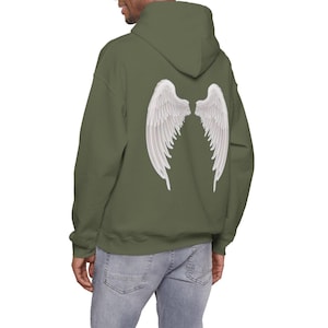 May include: An olive green hoodie featuring a white angel wing design on the back. The hoodie has a hood and long sleeves. The model is wearing blue jeans.
