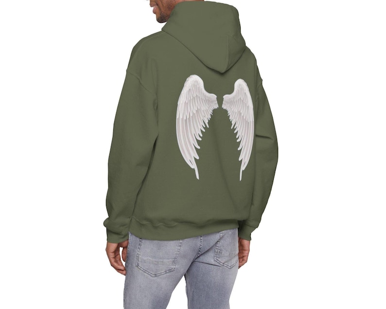May include: An olive green hoodie featuring a white angel wing design on the back. The hoodie has a hood and long sleeves. The model is wearing blue jeans.