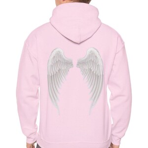 May include: A light pink hoodie with a hood and white angel wings printed on the back. The wings are detailed with individual feathers, creating a realistic appearance. The hoodie is a casual garment.