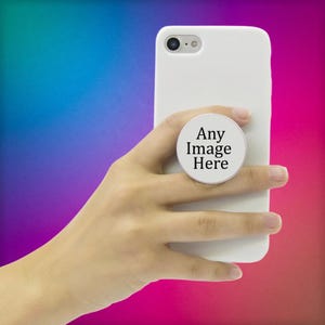 May include: A white smartphone case featuring a circular, collapsible phone grip attached to the back. The center of the circular grip is white and displays the black text Any Image Here in a clear, sans-serif font, centered on the surface.
