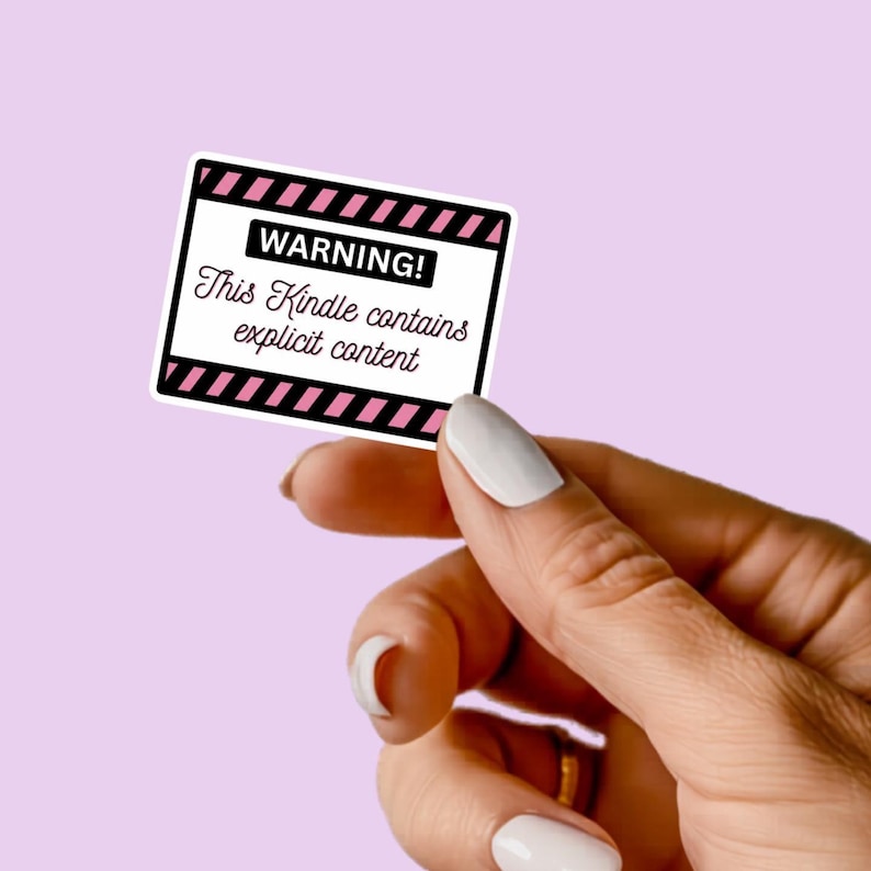 May include: A white sticker with a black border and pink diagonal stripes. The sticker has the word "WARNING!" at the top and the text "This Kindle contains explicit content" below. The sticker is held against a light purple background.