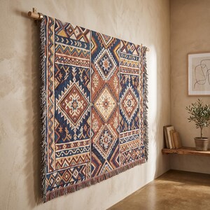 May include: A rectangular woven wall hanging featuring a geometric pattern in shades of navy blue, burnt orange, cream, and mustard yellow. The textile displays repeating diamond and chevron motifs with a fringed edge, suspended from a wooden rod.