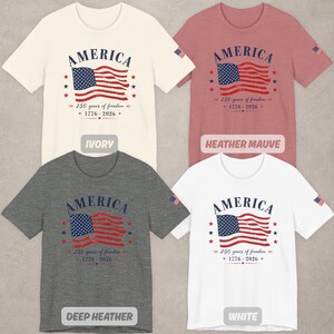 May include: Four short-sleeve t-shirts in ivory, heather mauve, deep heather, and white. Each shirt features a graphic of an American flag with the text AMERICA, 250 years of freedom, and 1776-2026. A small American flag is printed on the left sleeve.