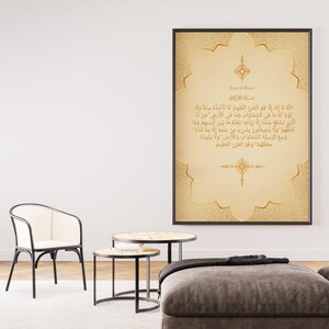 Puede incluir: Una obra de arte enmarcada con caligrafía árabe dorada sobre un fondo beige. El marco es negro. La obra se exhibe en un salón, junto con una silla, mesas auxiliares y una planta en maceta.