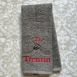 May include: Gray hand towel with red embroidered hockey sticks, a puck, and the number 21. The name "Trentin" is also embroidered in red.