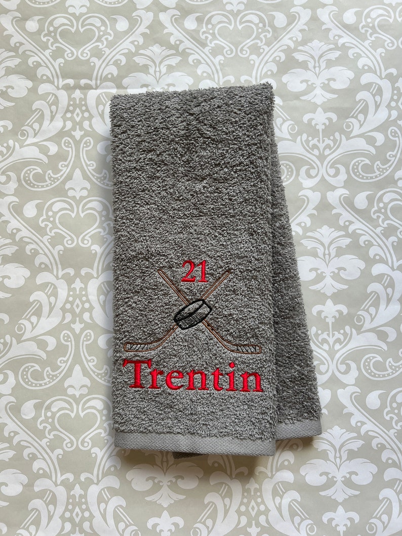 May include: Gray hand towel with red embroidered hockey sticks, a puck, and the number 21. The name "Trentin" is also embroidered in red.