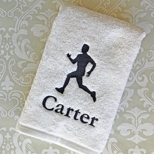 May include: White hand towel with a black silhouette of a runner and the name "Carter" embroidered in black. The text "This towel is stitched in black" is at the bottom of the image.