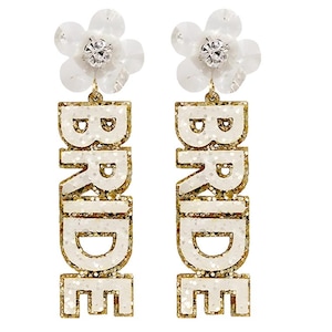 May include: Dangling earrings with a white flower and a sparkling center. The word "BRIDE" is spelled out in gold glitter letters. A festive accessory for a wedding.