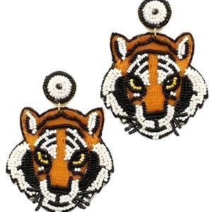 May include: A pair of dangle earrings featuring tiger head motifs crafted with intricate beadwork. The tigers are rendered in shades of orange, black, and white, with yellow eyes. Each earring includes a circular stud top with white and black beads.