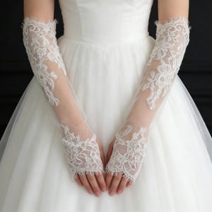 May include: Delicate white lace bridal gloves. The gloves showcase detailed floral lace designs and reach the upper arm. The sheer material allows the skin to be seen, producing a refined and romantic appearance. Ideal for weddings or special events.