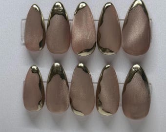 May include: Set of ten almond-shaped false nails. Each nail is a light brown color with a metallic gold trim along the tip. The nails are arranged in two rows of five.