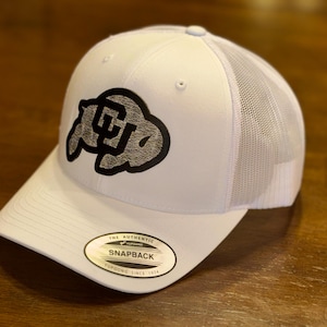 Puede incluir: Gorra de camionero blanca con un logotipo negro y gris en la parte delantera. La gorra tiene una parte trasera de malla y un cierre a presión. La visera es curva y una pequeña etiqueta dice "The Authentic Snapback".