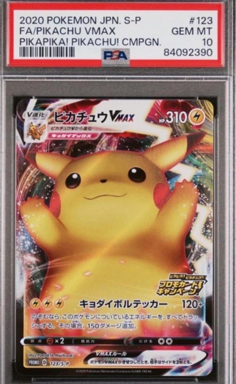 May include: A white ceramic mug with a black handle and the text "But First, Coffee" in a bold, black font. The mug is set against a blurred background. The mug appears to be approximately 10 cm tall.