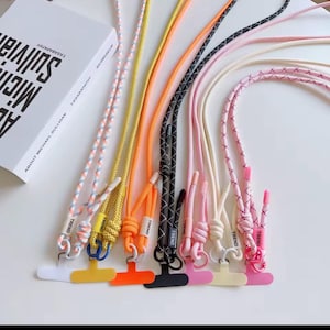 Può includere: Una collezione di cordini colorati per telefono con vari design di corda e attacchi in plastica. I cordini presentano una gamma di colori, tra cui arancione, giallo, rosa e nero. Ogni cordino ha la parola "TREND" stampata.
