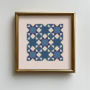 May include: Framed cross-stitch artwork featuring a geometric pattern in shades of blue, cream, and purple. The design includes squares, diamonds, and star-like shapes. The artwork is set against a light pink background and framed in a gold-colored frame.