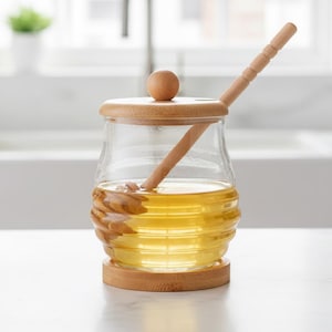 May include: A glass honey jar with a wooden lid and dipper. The jar is filled with golden honey and sits on a wooden base. The jar has a capacity of 300ml.