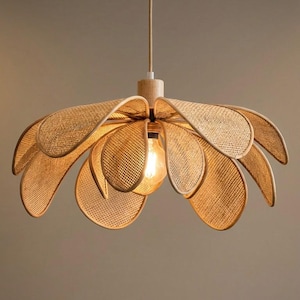 May include: A hanging pendant light fixture featuring a flower-shaped shade constructed from light brown woven rattan. The shade consists of multiple overlapping petal-like panels arranged around a central light bulb and a light wood mounting base.