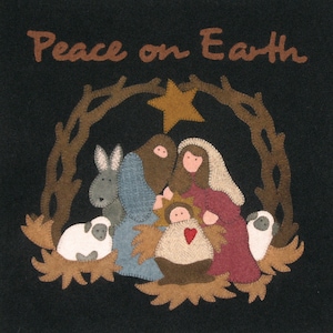 May include: A felt Christmas ornament depicting the nativity scene with a star above the manger. The text "Peace on Earth" is at the top of the ornament.