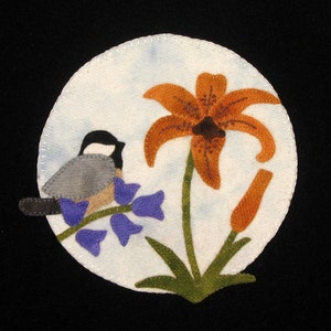以下が含まれることがあります： 白い背景に、紫の花が咲いた枝に止まっている小さな灰色の鳥と、緑の茎を持つ大きなオレンジ色のユリが描かれたフェルトのアップリケデザインです。