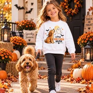 May include: A white long-sleeve sweatshirt featuring a graphic of a golden-coloured dog looking up at a ghost, with orange stars and black bats. The text reads Little Howl-o-ween Helper with a small paw print icon centred below the text.
