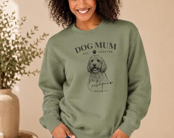 May include: An olive green crewneck sweatshirt featuring a dark graphic print of a Cockapoo dog. The text reads DOG MUM EST. FOREVER and Cockapoo CLUB with a small paw print and heart icon. The sweatshirt has long sleeves and ribbed cuffs.