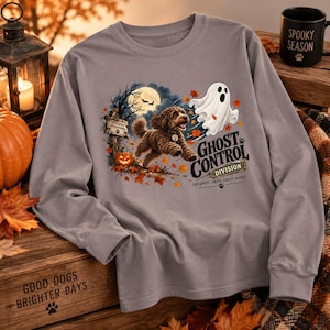 May include: A grey long-sleeve shirt featuring a graphic of a brown dog running toward a white ghost. The text reads GHOST CONTROL DIVISION, SEE GHOST, CHASE GHOST, REPEAT, and COCKAPOO OPERATIONS. The design includes a full moon, autumn leaves, and a pumpkin.