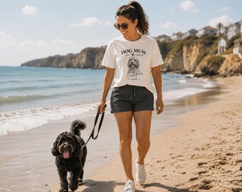 May include: A white short-sleeved t-shirt featuring a black line drawing of a dog and the text DOG MUM EST. FOREVER Cockapoo CLUB, paired with dark gray drawstring shorts. The shirt has a crew neckline and a relaxed fit, while the shorts are solid.