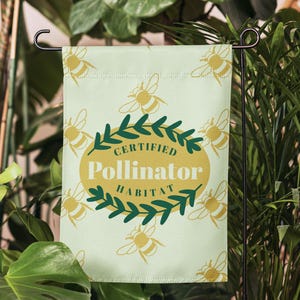 May include: A rectangular garden flag with a light green background featuring a repeating pattern of yellow bees. In the center, a yellow oval is surrounded by a green leafy wreath with the text "CERTIFIED Pollinator HABITAT" printed.