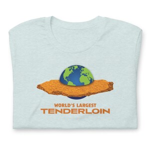 May include: Light blue t-shirt with a graphic of the Earth on a large, golden-brown tenderloin. The text "WORLD'S LARGEST TENDERLOIN" is printed in orange below the image. The shirt is folded.
