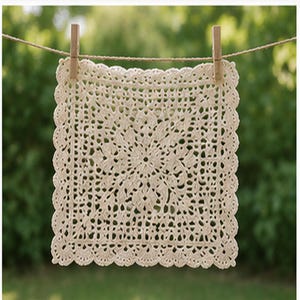 May include: A square, cream-colored crochet doily, suspended by a wooden clothespin on a string. The doily features an intricate floral pattern in the center and a scalloped edge. The background is a blurred green, suggesting an outdoor setting.