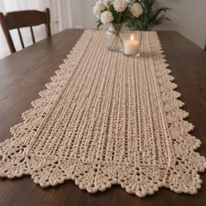 Puede incluir: Un camino de mesa rectangular de ganchillo en color beige que presenta un patrón texturizado de costillas verticales en el centro y un borde festoneado decorativo con intrincados motivos en forma de abanico en todo el perímetro.