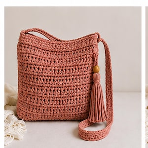 Può includere: Borsa a tracolla all'uncinetto rosa antico con una lunga tracolla e un nappa decorativa. La borsa presenta una trama intrecciata e un accento di perline di legno sulla nappa. La borsa è di forma quadrata.