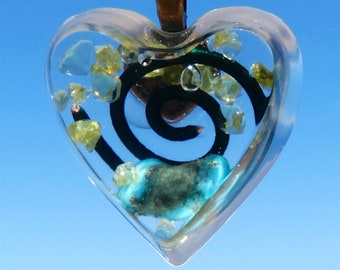 May include: A heart-shaped pendant with a clear resin design. The pendant features a spiral pattern with green and black accents, and small yellow and blue stones are embedded in the resin.