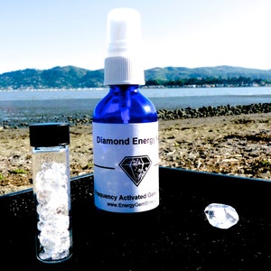 May include: A blue glass bottle with a white spray top and a white label that reads "Diamond Energy Water Frequency Activated Gem Elixir www.EnergyGemStore.com". A small clear glass vial filled with clear crystals and a clear diamond crystal are also pictured.