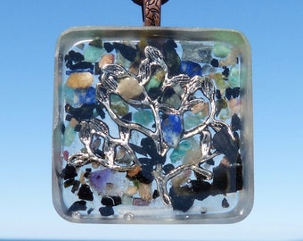 May include: A square pendant necklace with a silver tree design embedded in clear resin. The resin contains a variety of small, colorful stones and black specks.