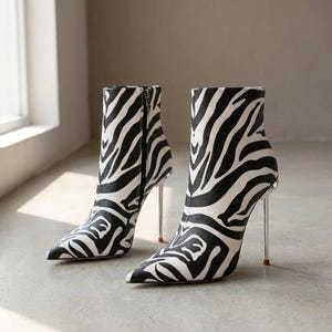 Peut inclure: Une paire de bottines avec un motif rayé zèbre noir et blanc. Les bottines présentent un bout pointu, un talon aiguille haut avec une finition argentée métallique et une fermeture éclair latérale sur le côté intérieur de la tige.