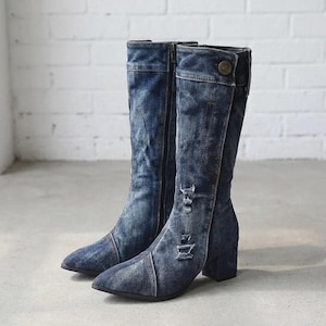 May include: A pair of mid-calf boots crafted from blue denim fabric with a distressed, acid-wash finish. These boots feature a pointed toe, a block heel, a side zipper closure, and a decorative button detail at the top of the shaft.