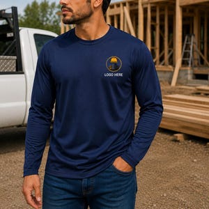 May include: Navy blue long-sleeved top with a crew neck and a small logo on the chest. The text "LOGO HERE" is visible. The person is wearing blue jeans. A white truck is in the background.